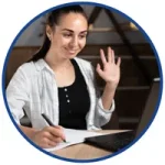 Szkolenia online z MS Excel i obsługi klienta – kobieta macha do kamery laptopa podczas rozmowy wideo i notuje