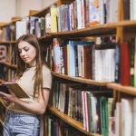 Szkolenia i webinary dla instytucji kultury – kobieta czyta książkę między regałami w bibliotece