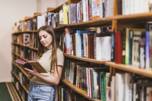 Szkolenia i webinary dla instytucji kultury – kobieta czyta książkę między regałami w bibliotece