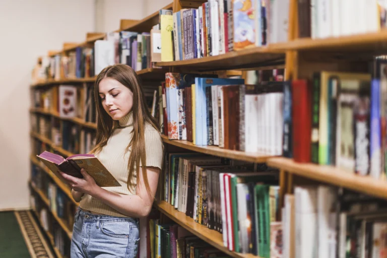 Szkolenia i webinary dla instytucji kultury – kobieta czyta książkę między regałami w bibliotece