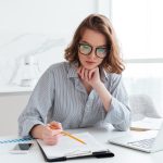 Young concentrated businesswoman in glasses and striped shirt wo