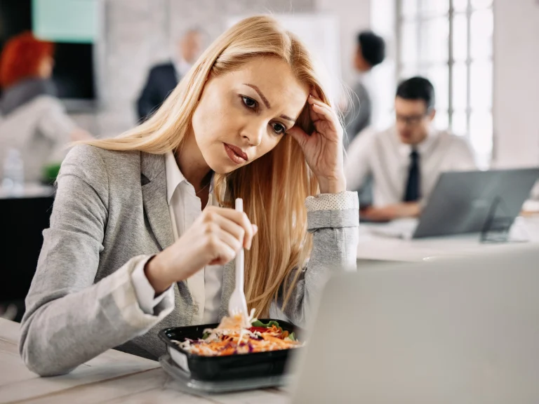 Przerwy w czasie pracy, wymogi prawne i praktyki w firmach – pracownica je sałatkę przy laptopie w biurze