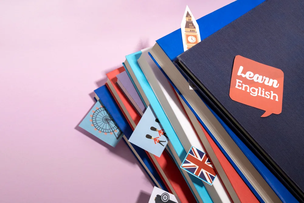 Stos podręczników do nauki języka angielskiego z naklejką Learn English i flagą Wielkiej Brytanii